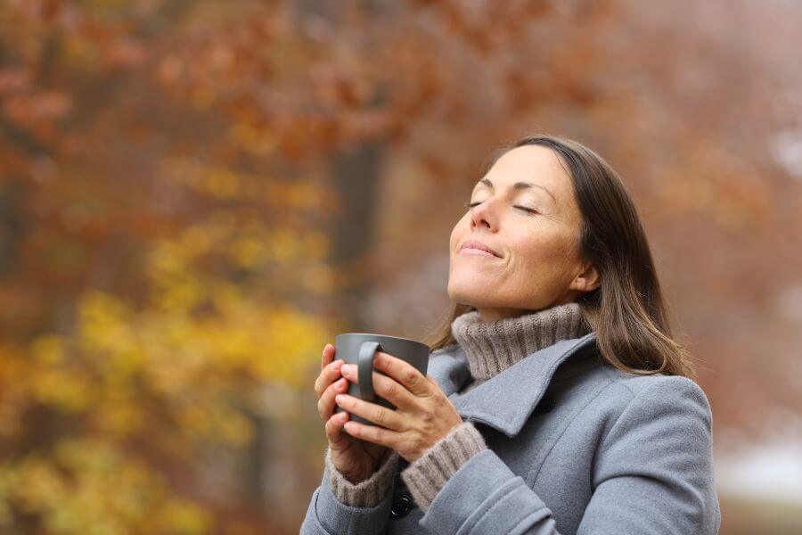 Woman holding warm cup in autumn setting to de-stress with mother nature.