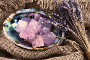 The Amazing Healing Benefits of Crystals Burlap background with a colorful shell with raw quartz crystals piled inside. A bunch of dry lavender sits to the side.