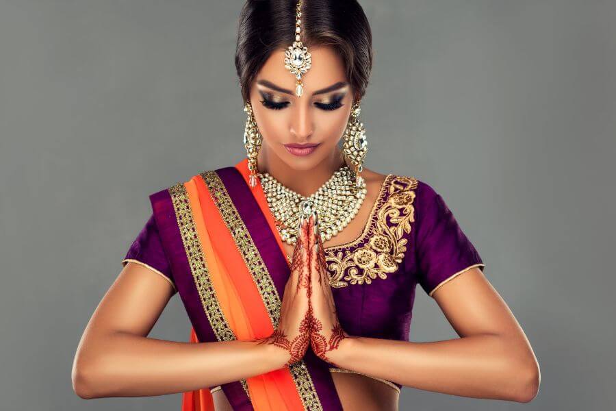 Woman from India in traditional attire with head bowed and hands in Namaste position.