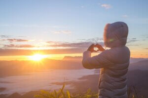 7 Steps to Becoming a Powerful Manifestor. Woman looking at sunset with her hands in a heart formation.